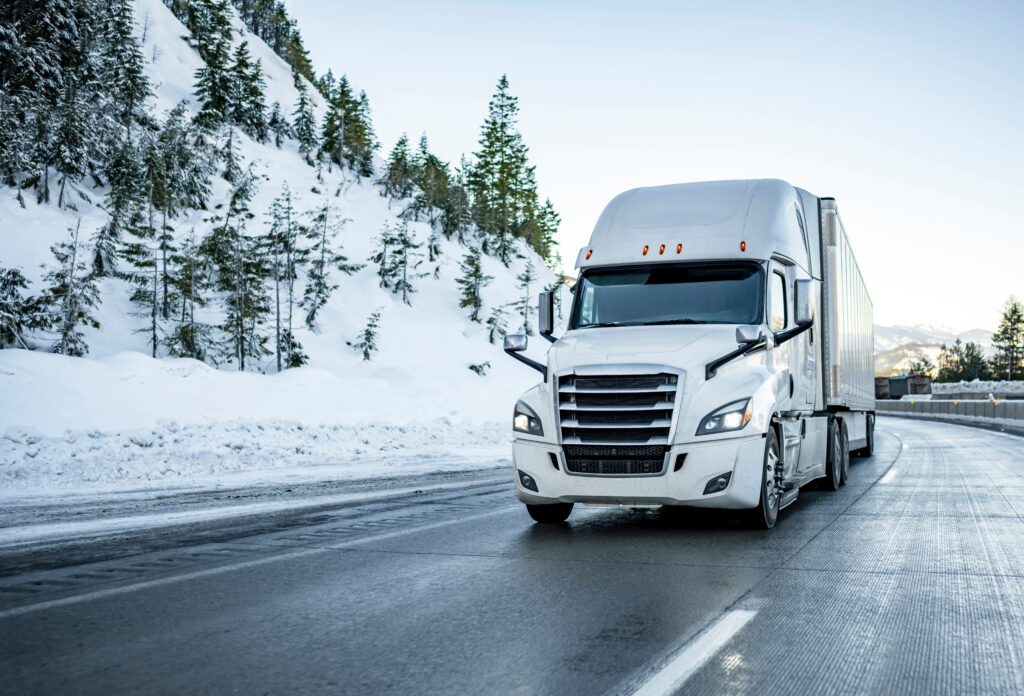 trucking fleet vehicle driving down highway in winter with snow and trees in the background